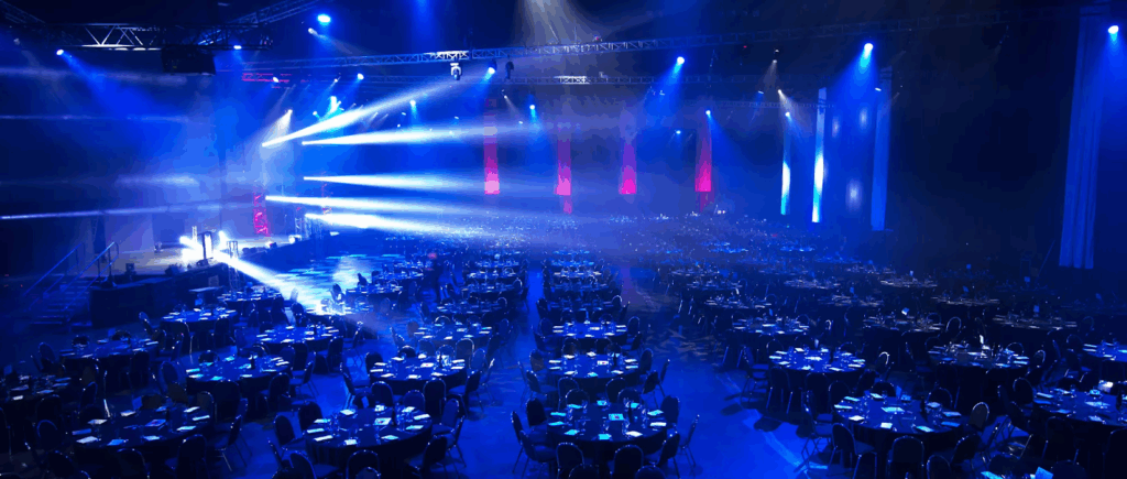 Corporate event ballroom with stage truss, professional AV lighting, banquet seating, and large-scale event production